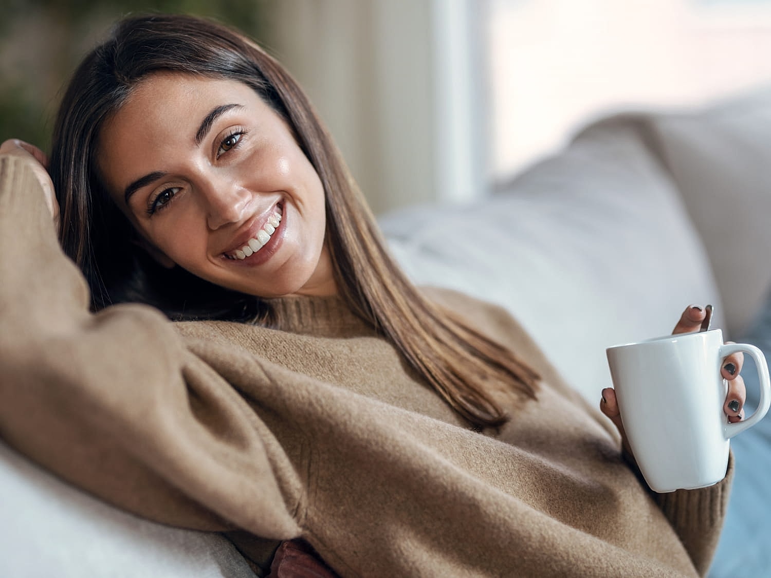 Smiling woman enjoying coffee on the couch.