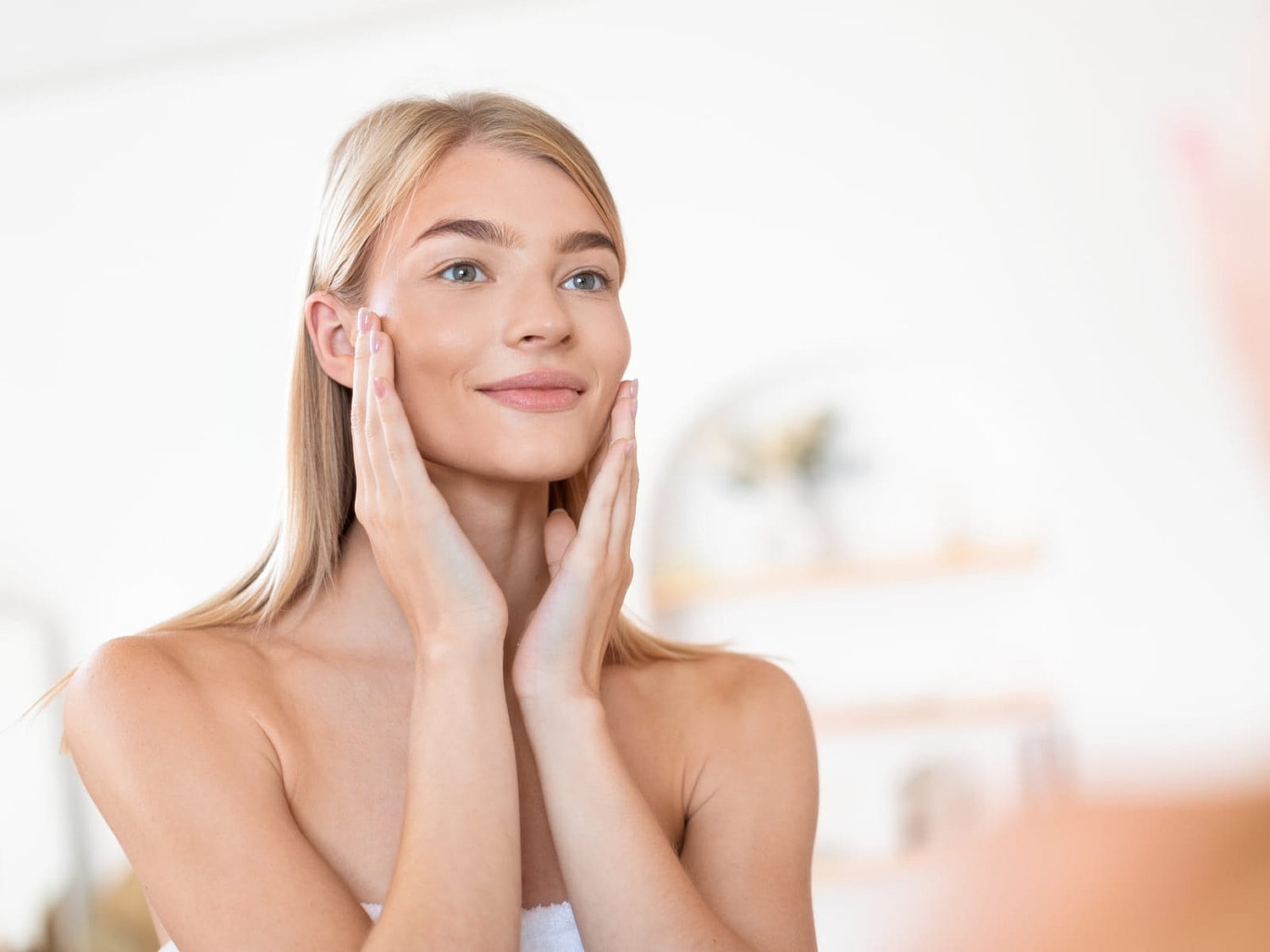 Woman applying skincare in front of a mirror.